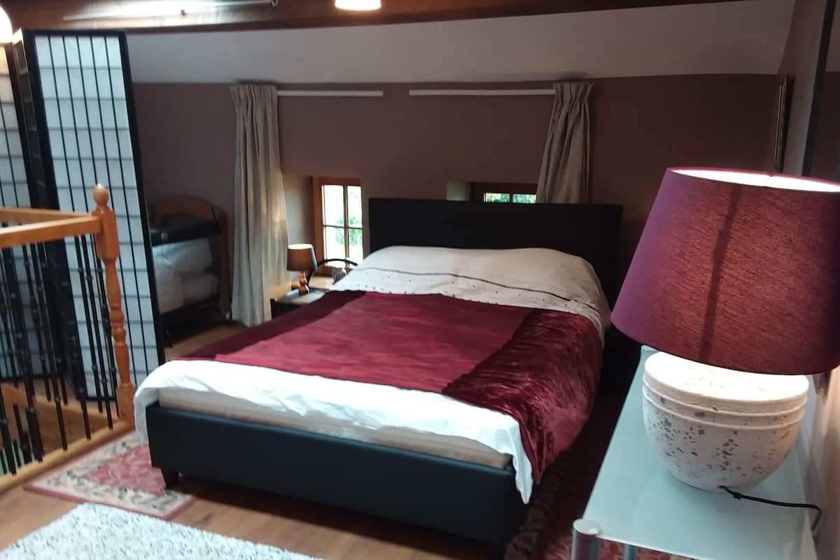 A bedroom with a bed, a nightstand, a lamp, and a window.