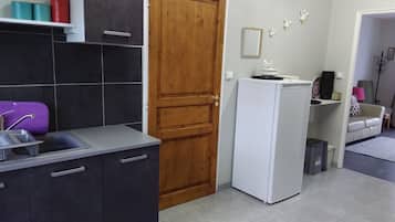 A kitchen with dark cabinets, a wooden door, a white refrigerator, and a sink with a purple dish rack.