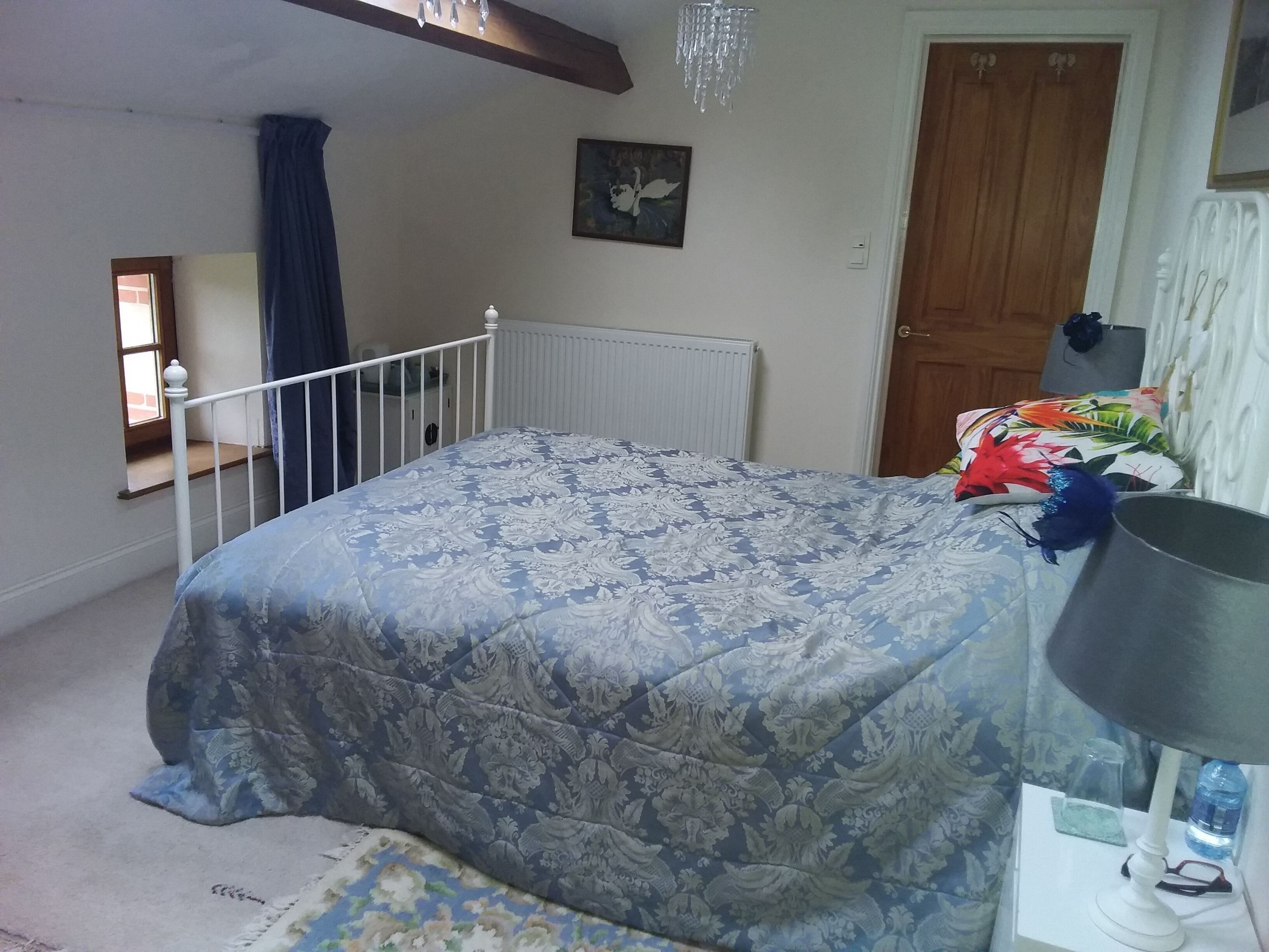 A bedroom with a bed, a nightstand, a radiator, a door, and a window with curtains.