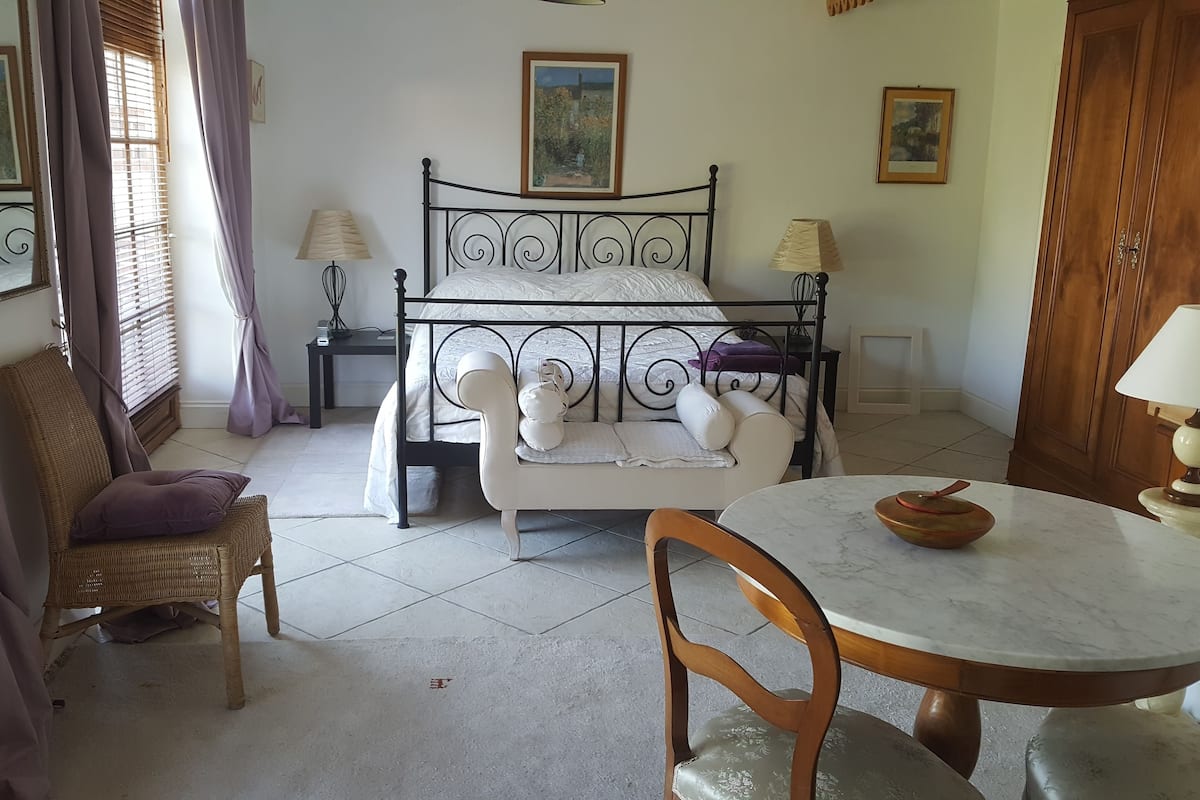 A bedroom with a bed, a chair, a table, and a window with curtains.
