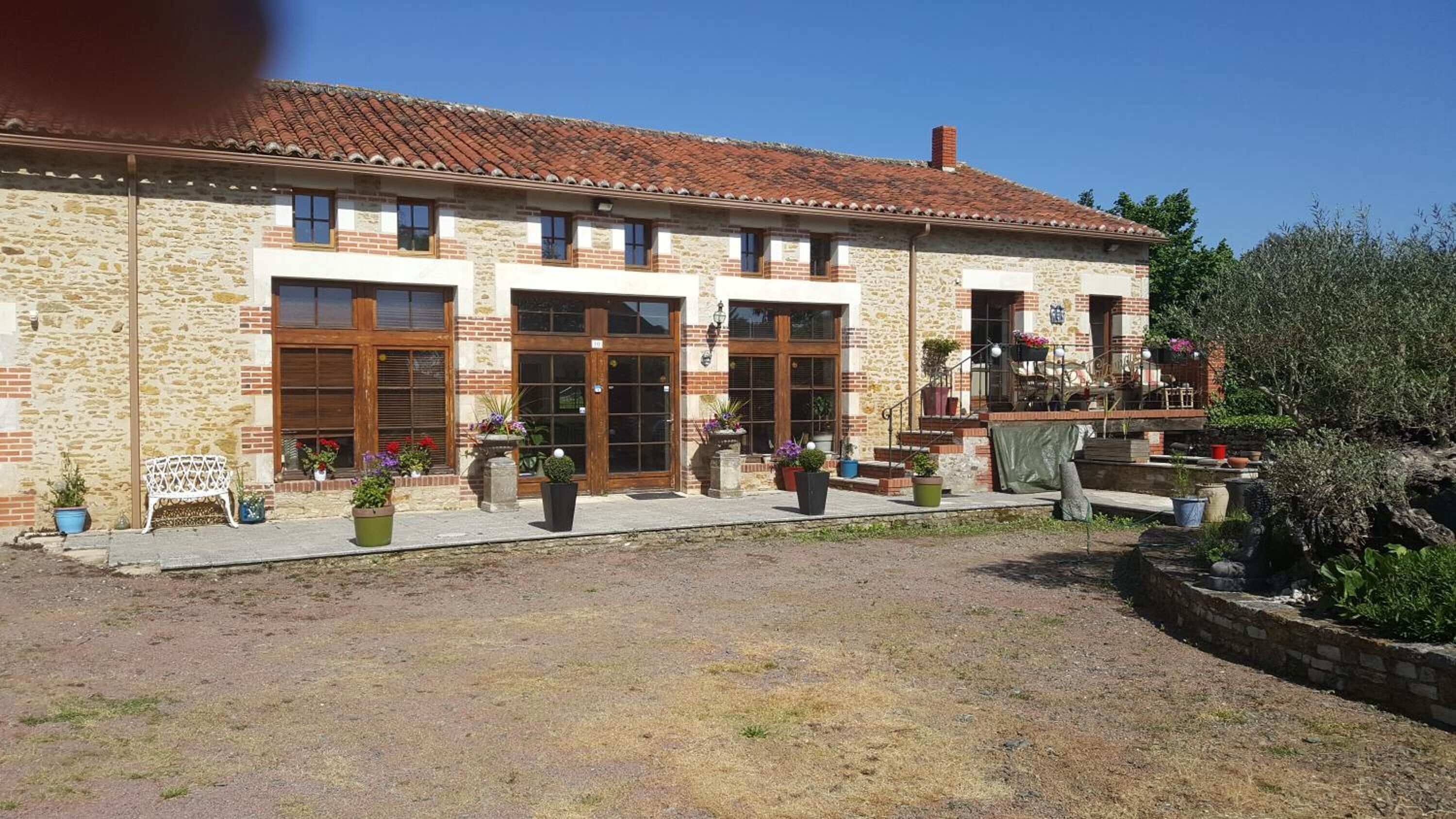 Un edificio de piedra con grandes puertas de madera, un pequeño balcón con plantas en macetas y un patio de grava.