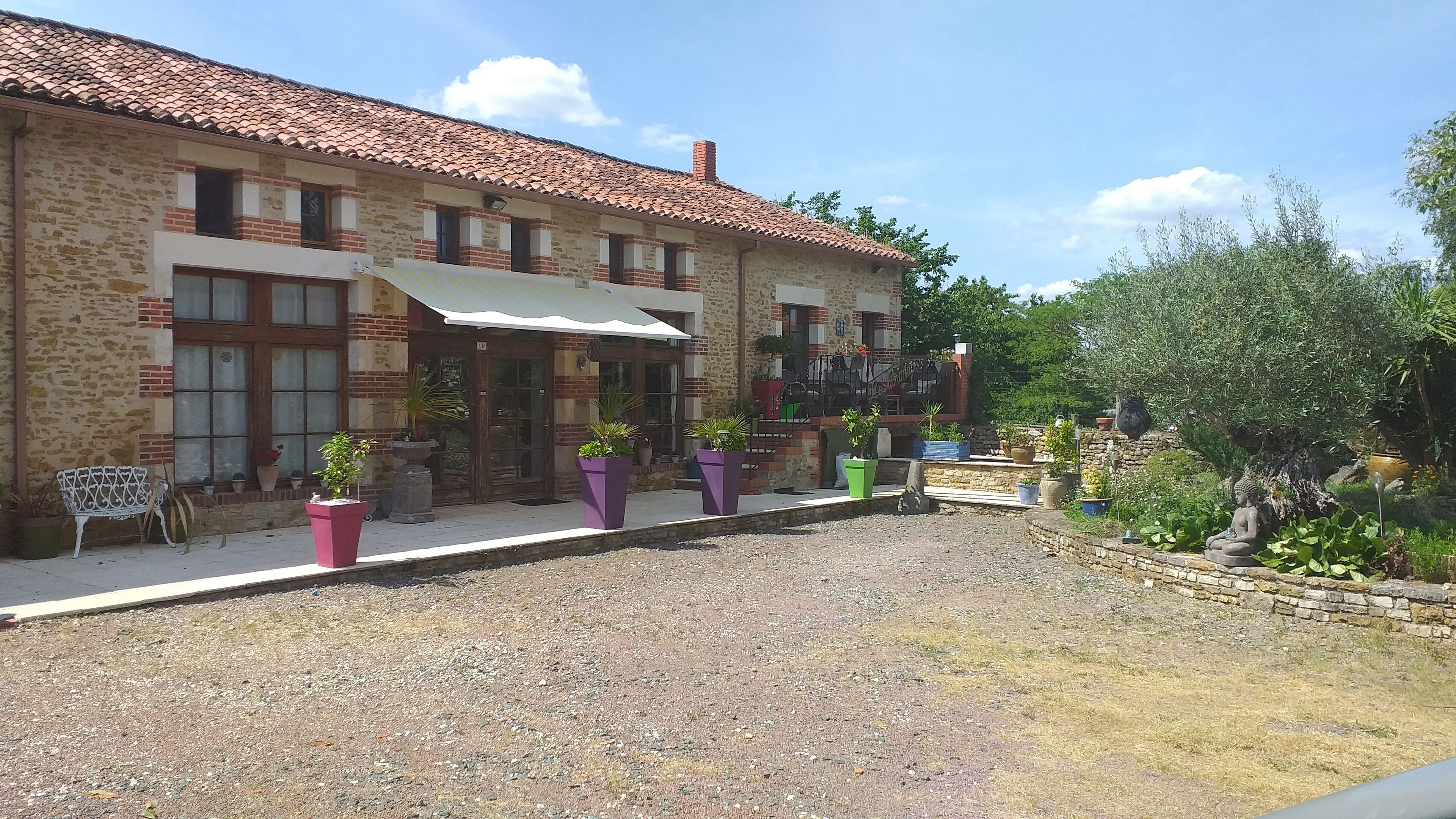 A stone building with a tiled roof, a covered patio area, and potted plants.
