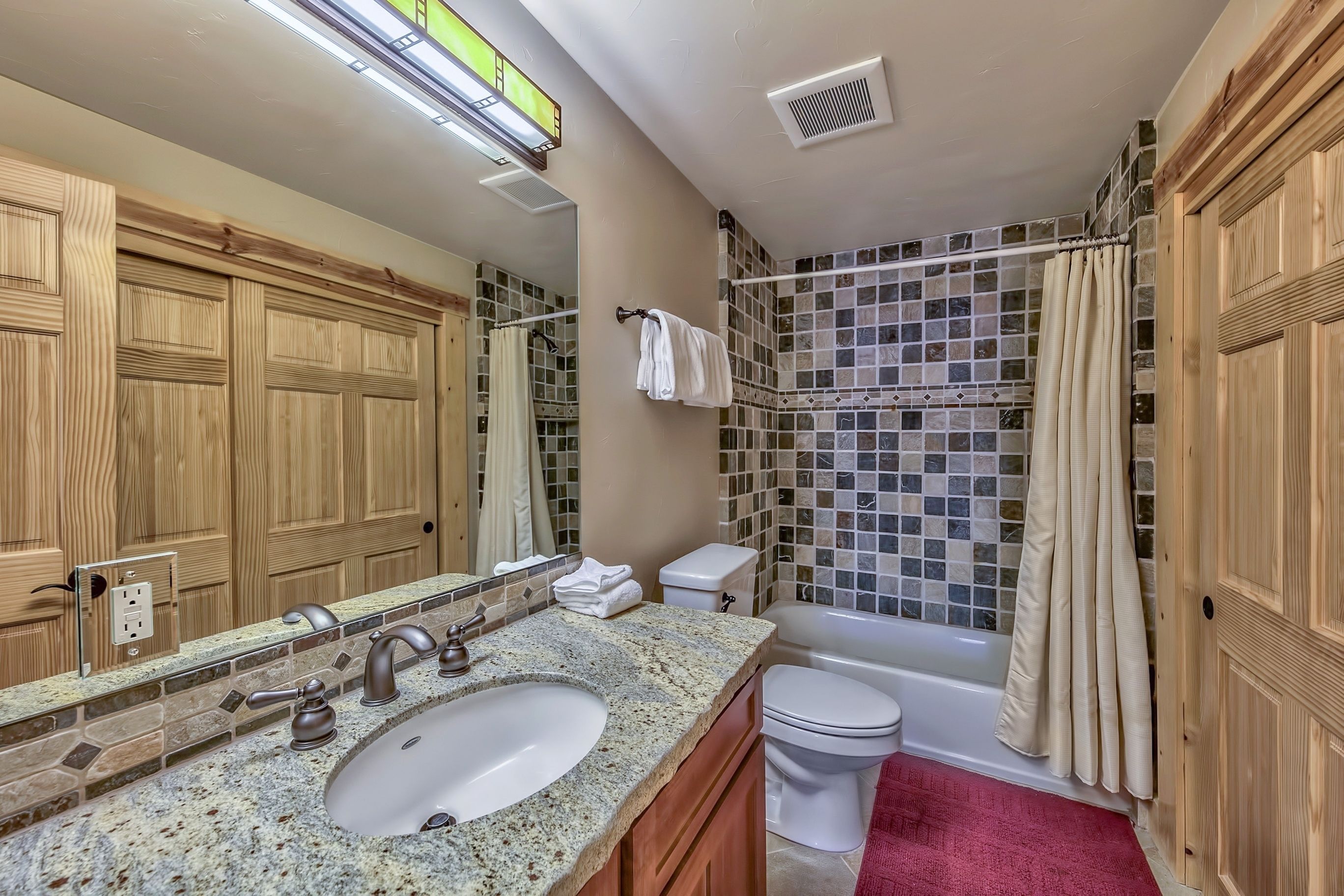 Ein Badezimmer mit Marmorwaschbecken, Holzschränken, einer weißen Toilette, einer Badewanne und einer Dusche mit Mosaikfliesen.