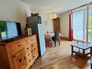 Um espaço de estar compacto com penteadeira de madeira, televisão, mesa de jantar com cadeiras e janela com cortinas.