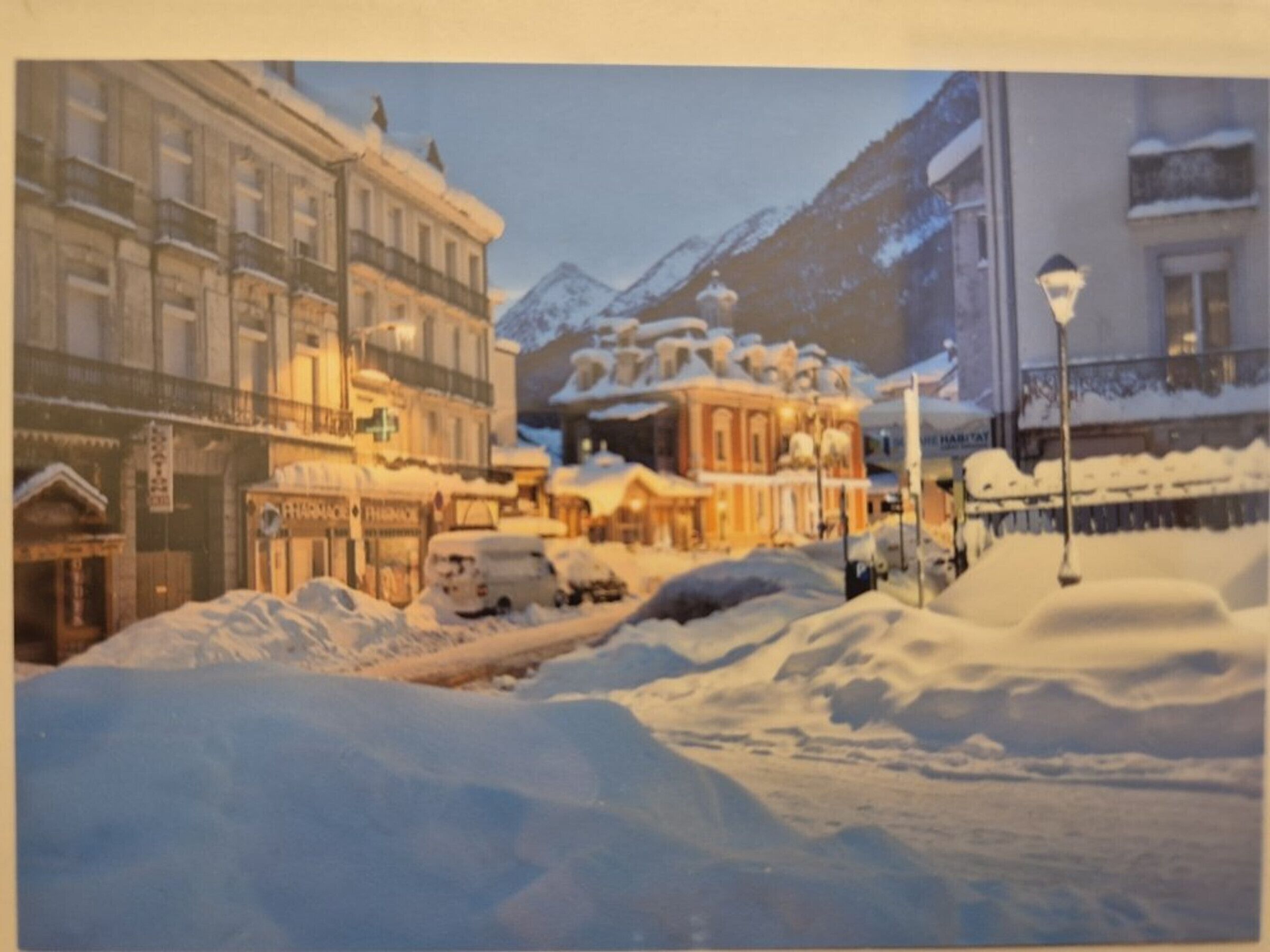 A snowy street scene with buildings and a mountain in the background.