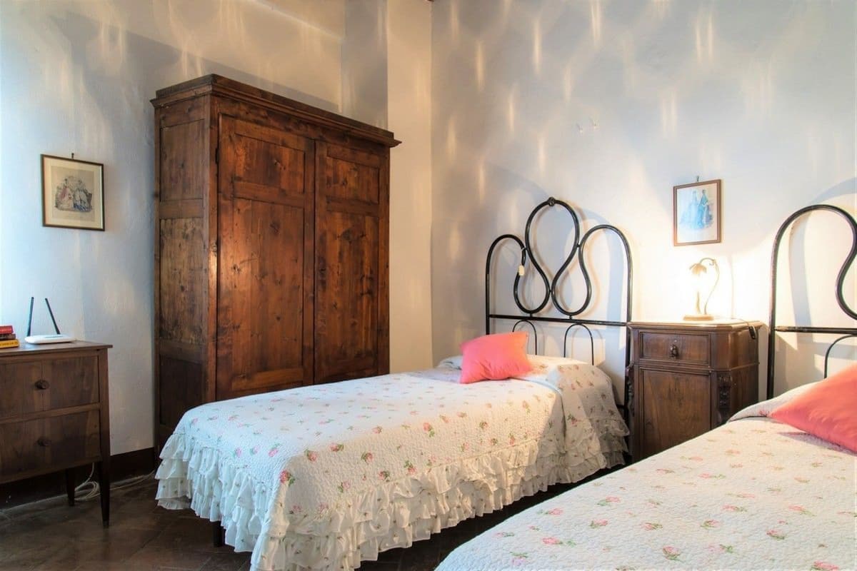 A bedroom with two beds, a wooden wardrobe, and a nightstand with a lamp.