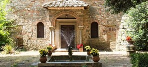 A stone building with a fountain, arched doorway, and potted plants. - Residenza d'epoca Il Cassero (Lucignano)