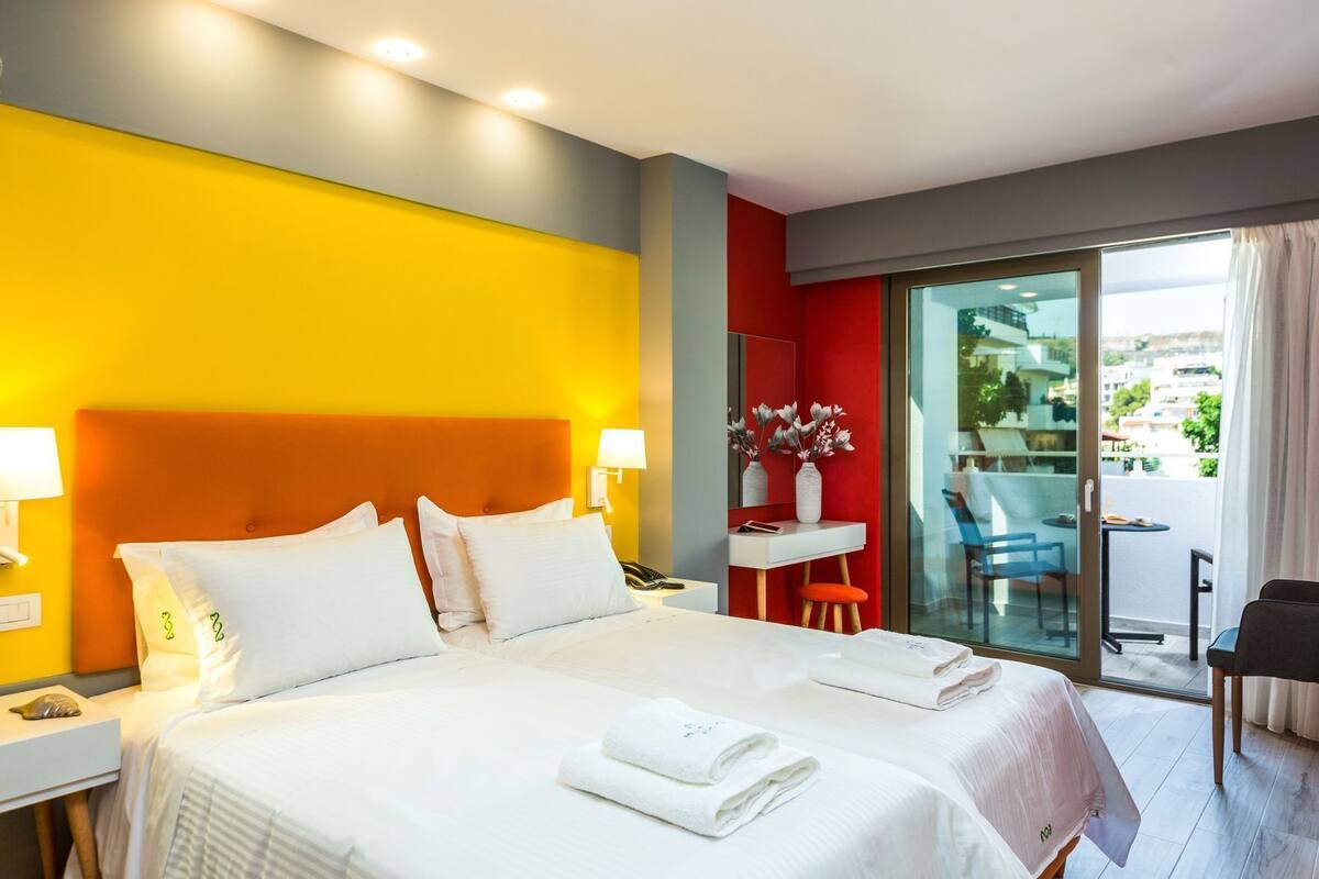 Una habitación de hotel con cama, mesitas de noche, escritorio, silla y balcón con vistas.