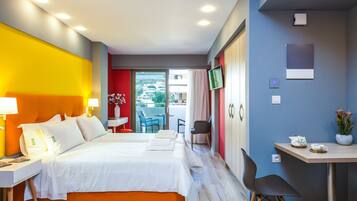 Habitación de hotel con cama, escritorio, silla, televisión y balcón con vista a edificios.
