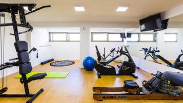 Un gimnasio con equipo de ejercicio variado, incluyendo una máquina de remo, pelotas de gimnasia y una banca.