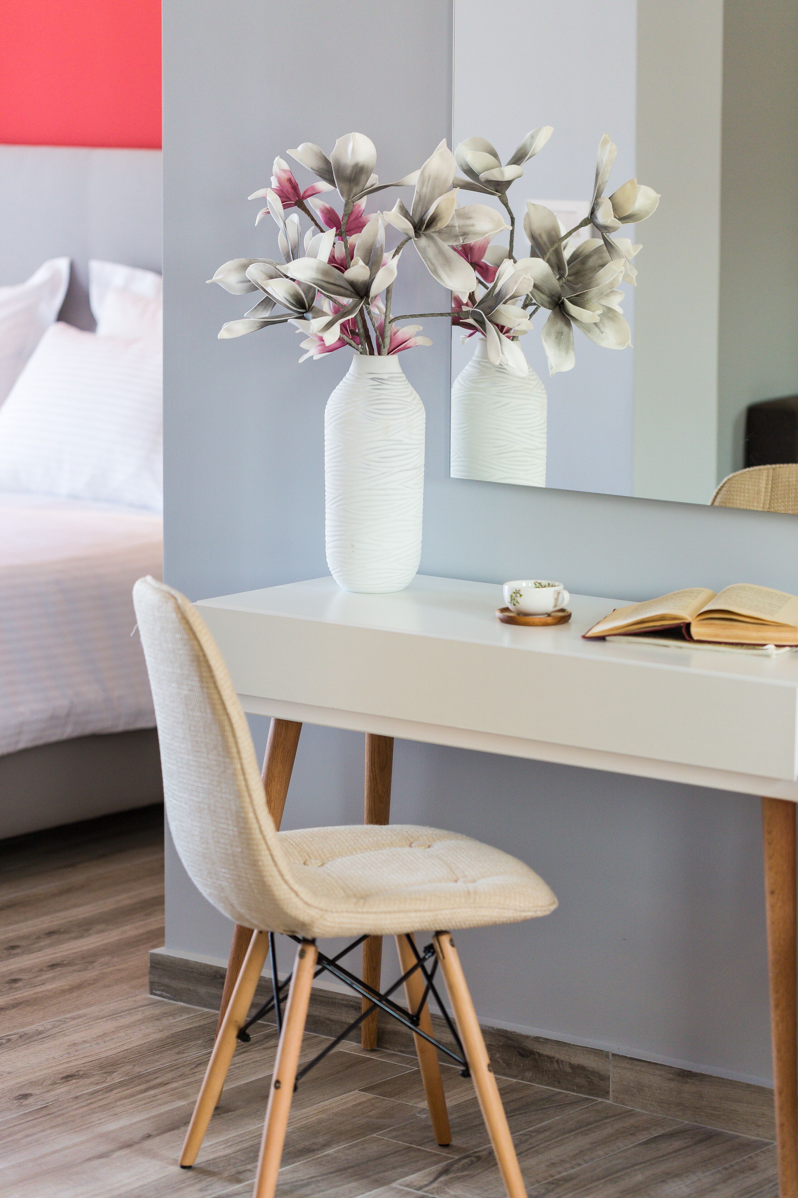 Une chambre à coucher moderne avec un bureau blanc, une chaise, un vase de fleurs et un livre.