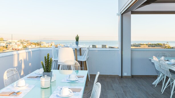 Un balcón con una mesa para dos, sillas, una planta en maceta y vista al mar.