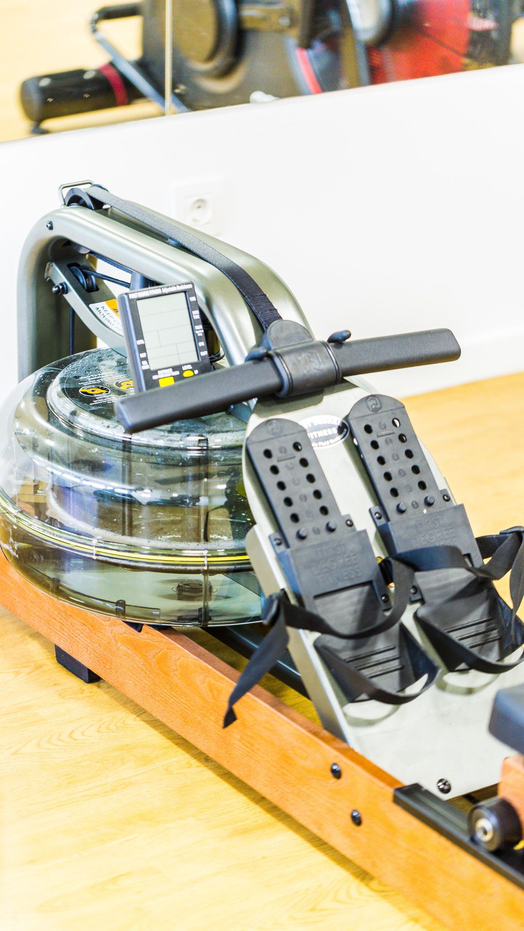 A stationary exercise bike with a digital display, foot pedals, and a wooden base.