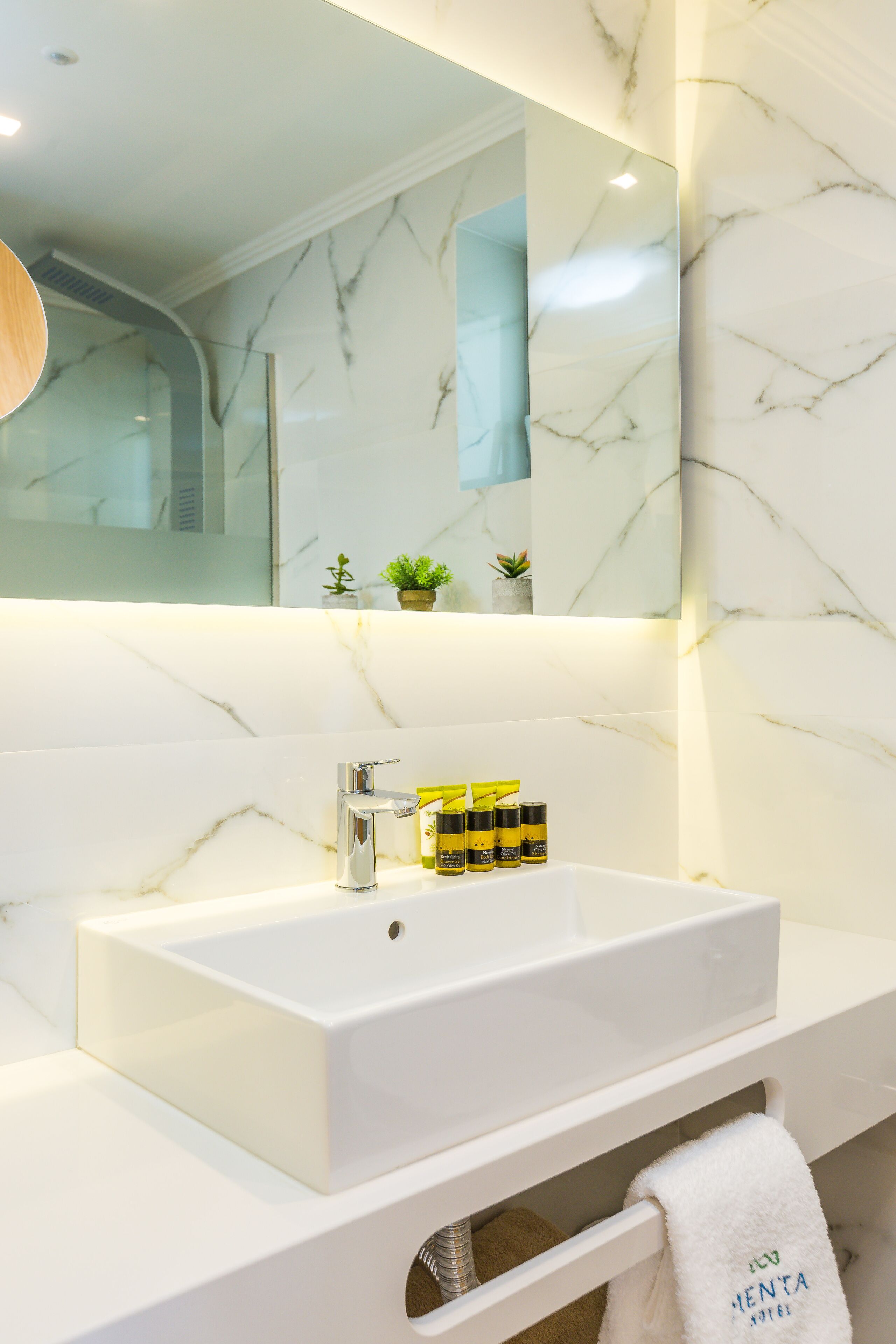 A modern bathroom with a white marble sink, a mirror, and a towel rack.