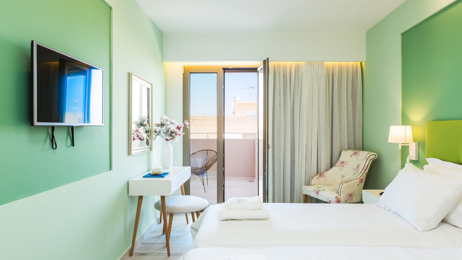 A hotel room with a bed, a desk, a chair, a TV, and a balcony with a view.