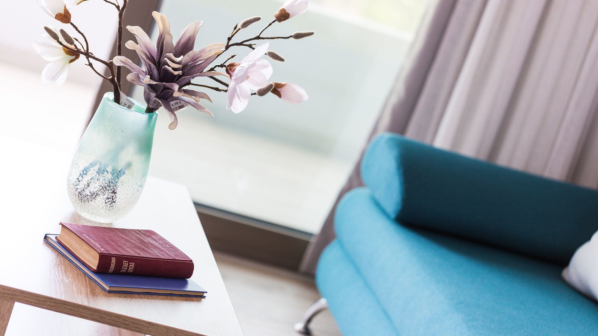 Una habitación con una mesa blanca, un jarrón con flores, un sofá azul y dos libros.