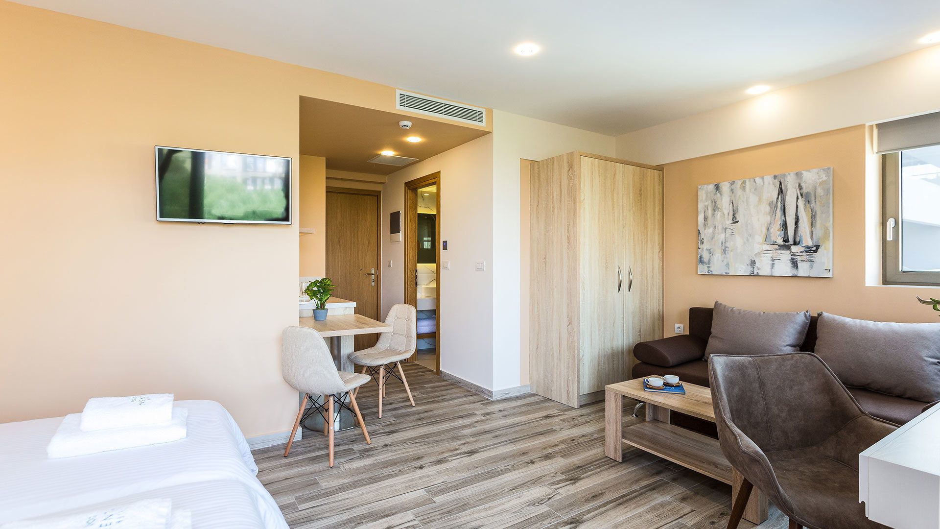 A modern hotel room with a bed, a sofa, a small table, and a TV.