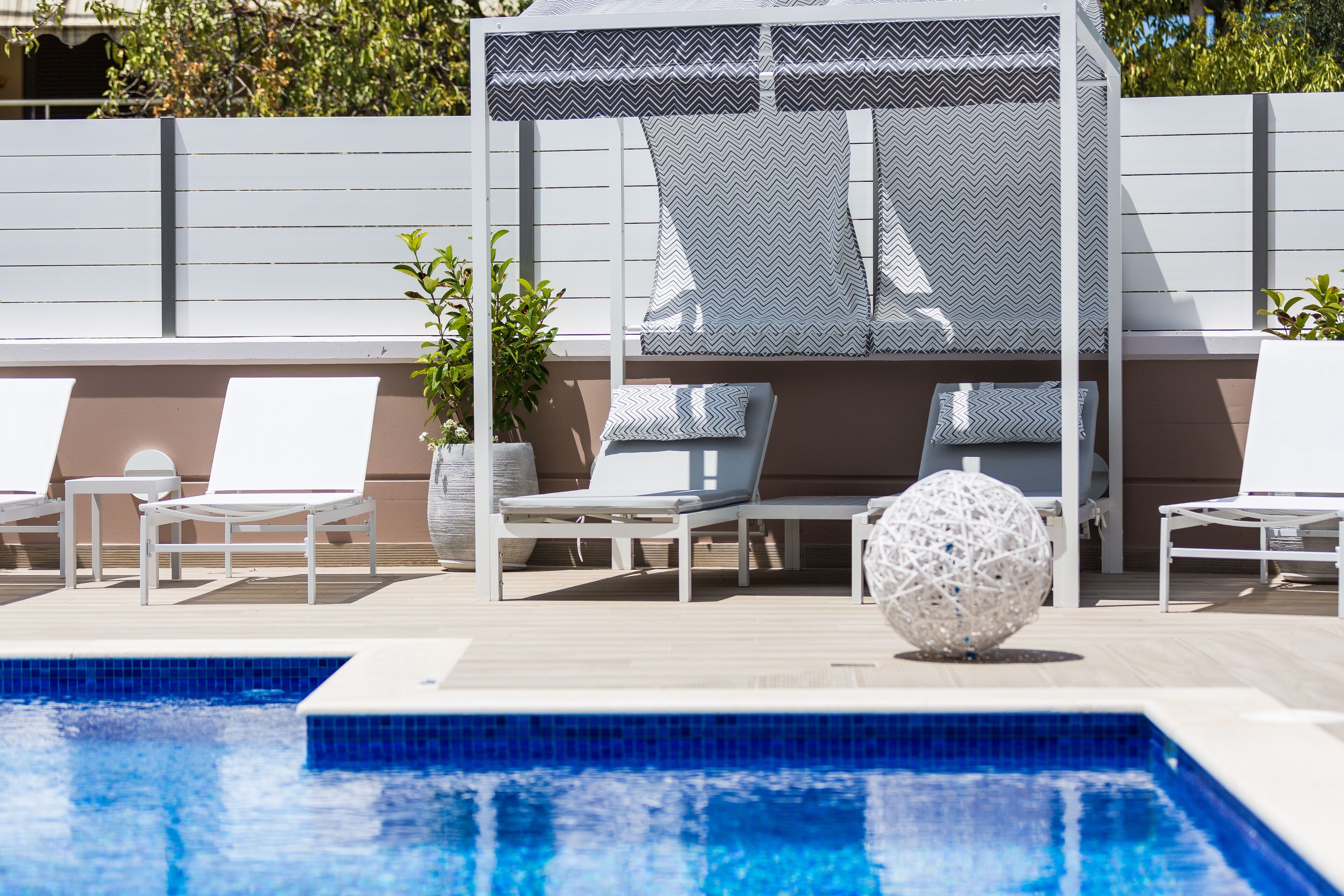 A pool area with lounge chairs, a covered seating area, and a decorative spherical object.