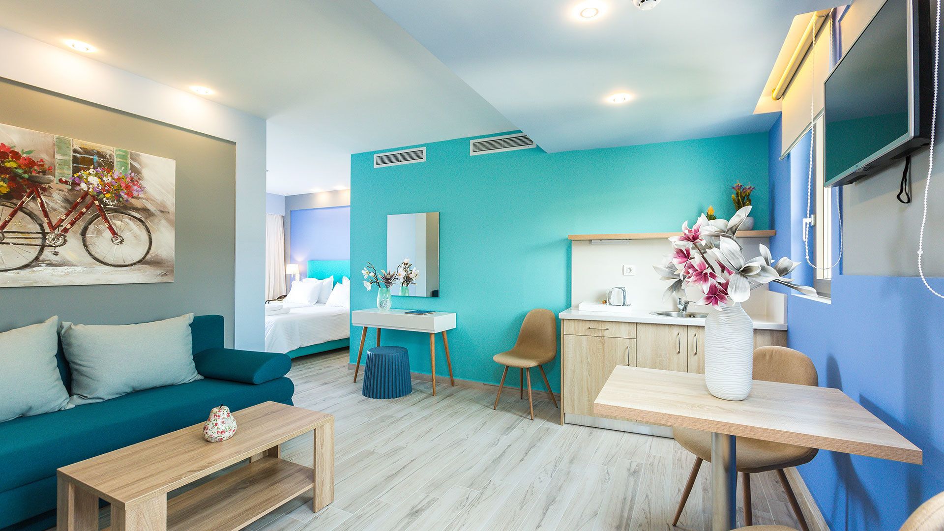 Une chambre d’hôtel moderne avec un mur d’accent de couleur turquoise, un lit, un bureau, une table basse et un coin salon.
