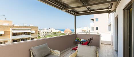 A balcony with wicker furniture, a small table, and a view of the sea and buildings.