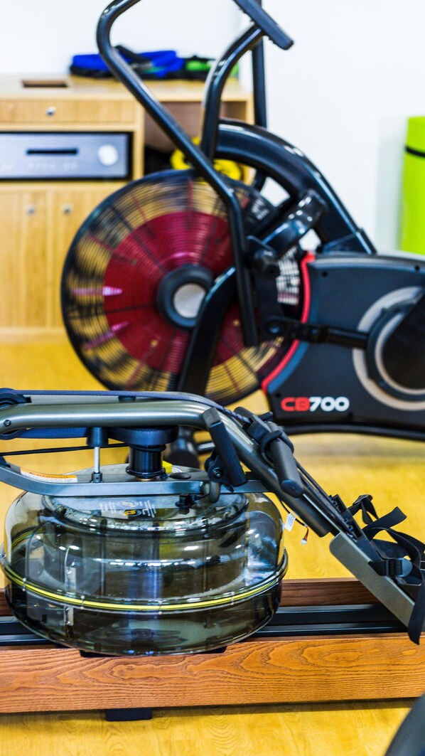 A stationary exercise bike with a digital display and a kettle on a wooden table.