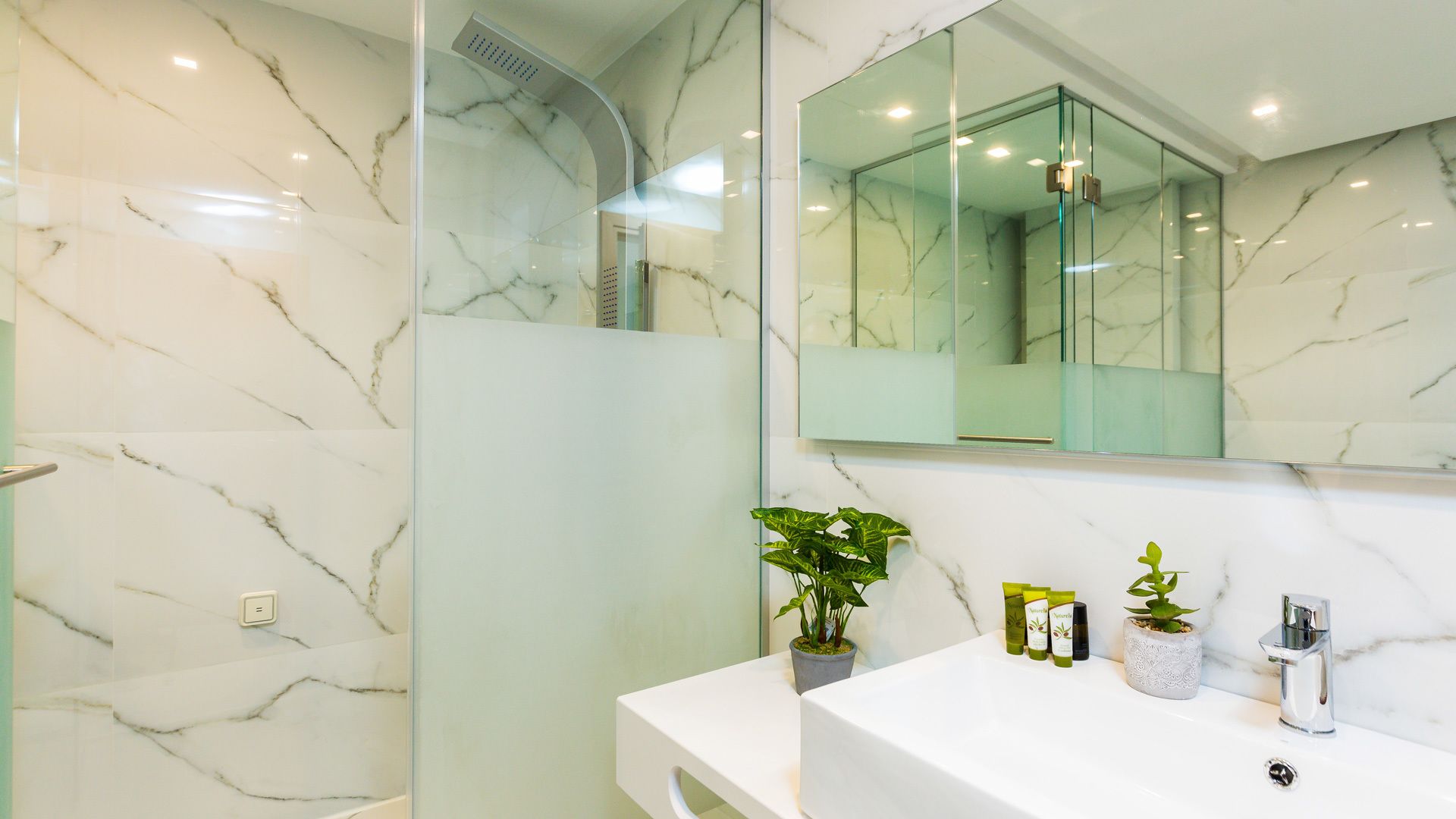 A modern bathroom with a marble floor, a glass shower enclosure, a white sink, and a large mirror.