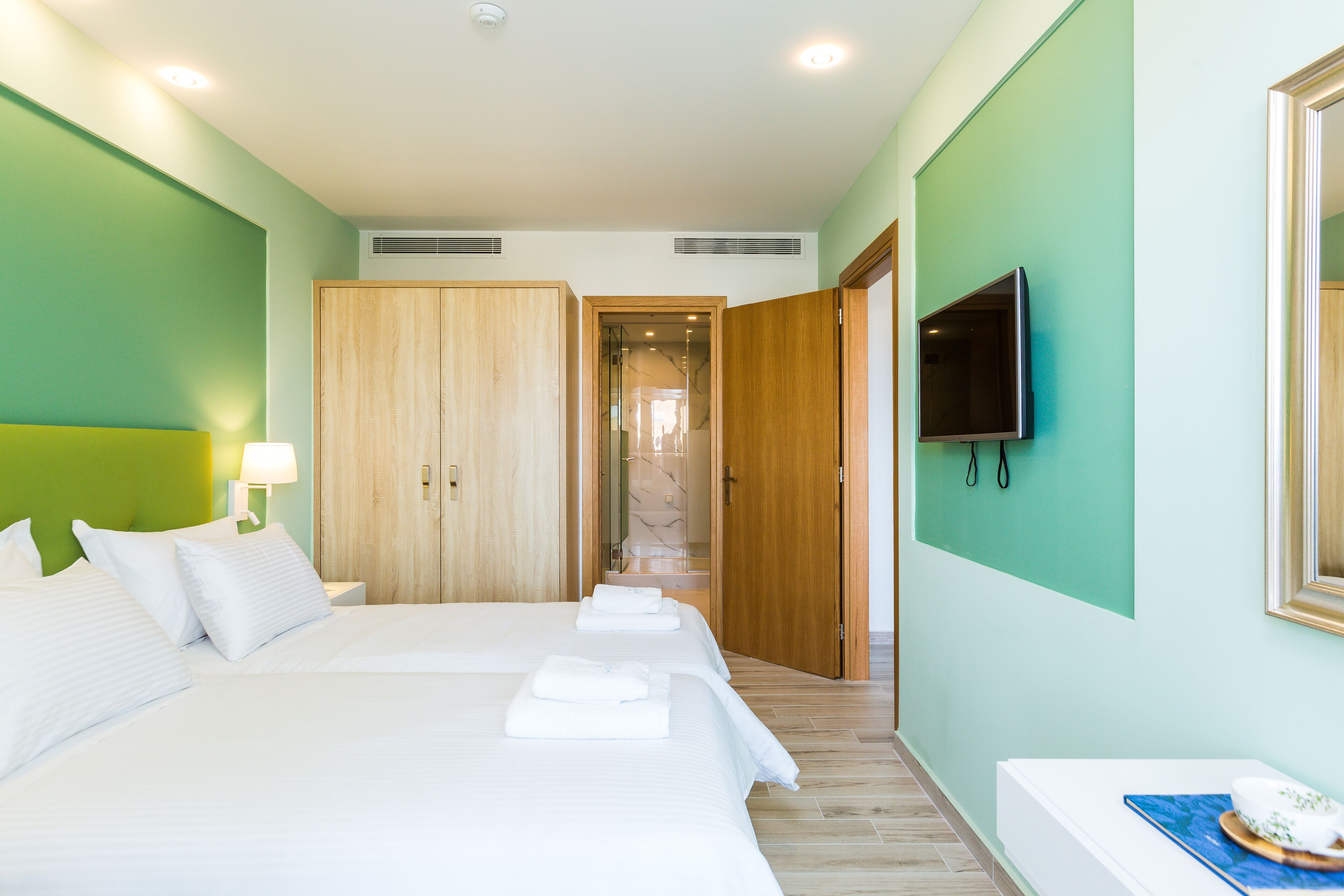 A hotel room with a large bed, a TV mounted on the wall, and a wooden wardrobe.