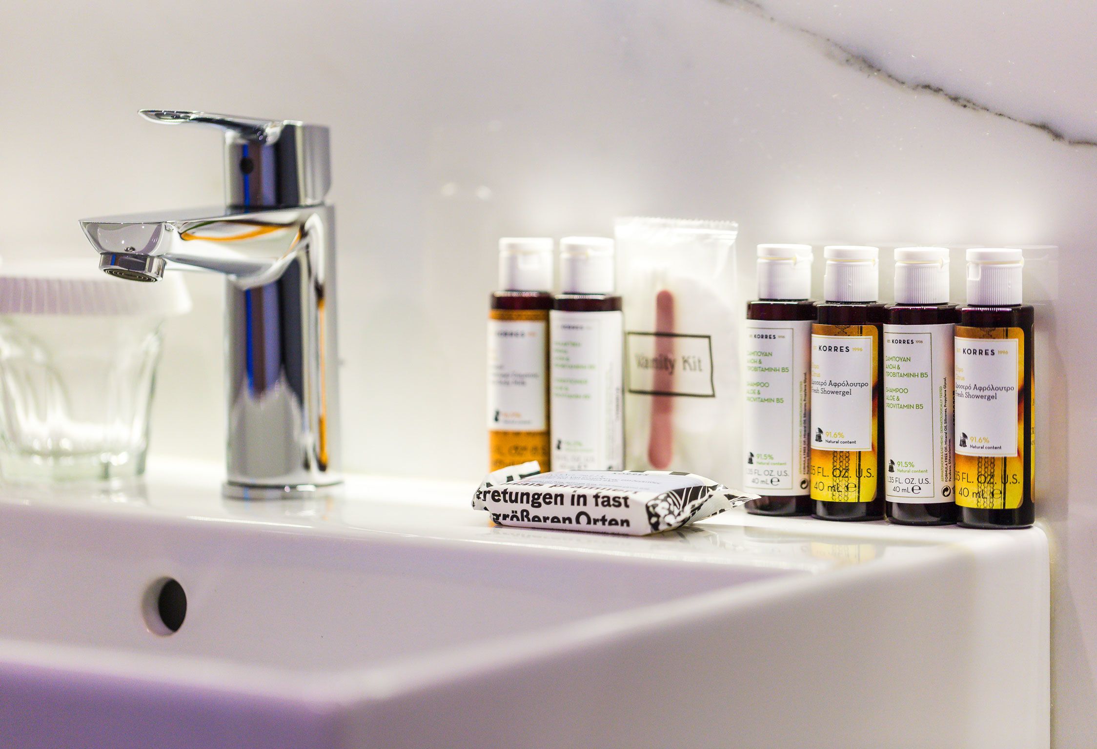 A bathroom sink with a chrome faucet, a glass, and several bottles of Korres shower gel.