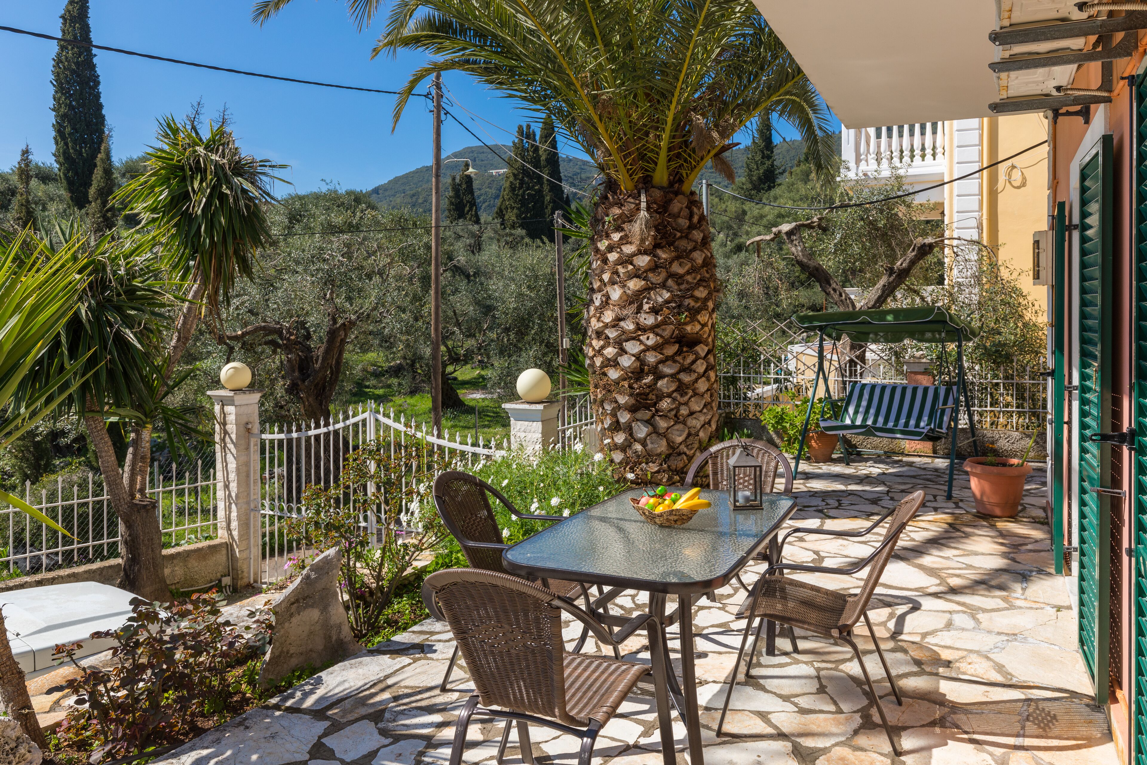 An outdoor patio with a table and chairs, surrounded by a stone floor and a white fence.