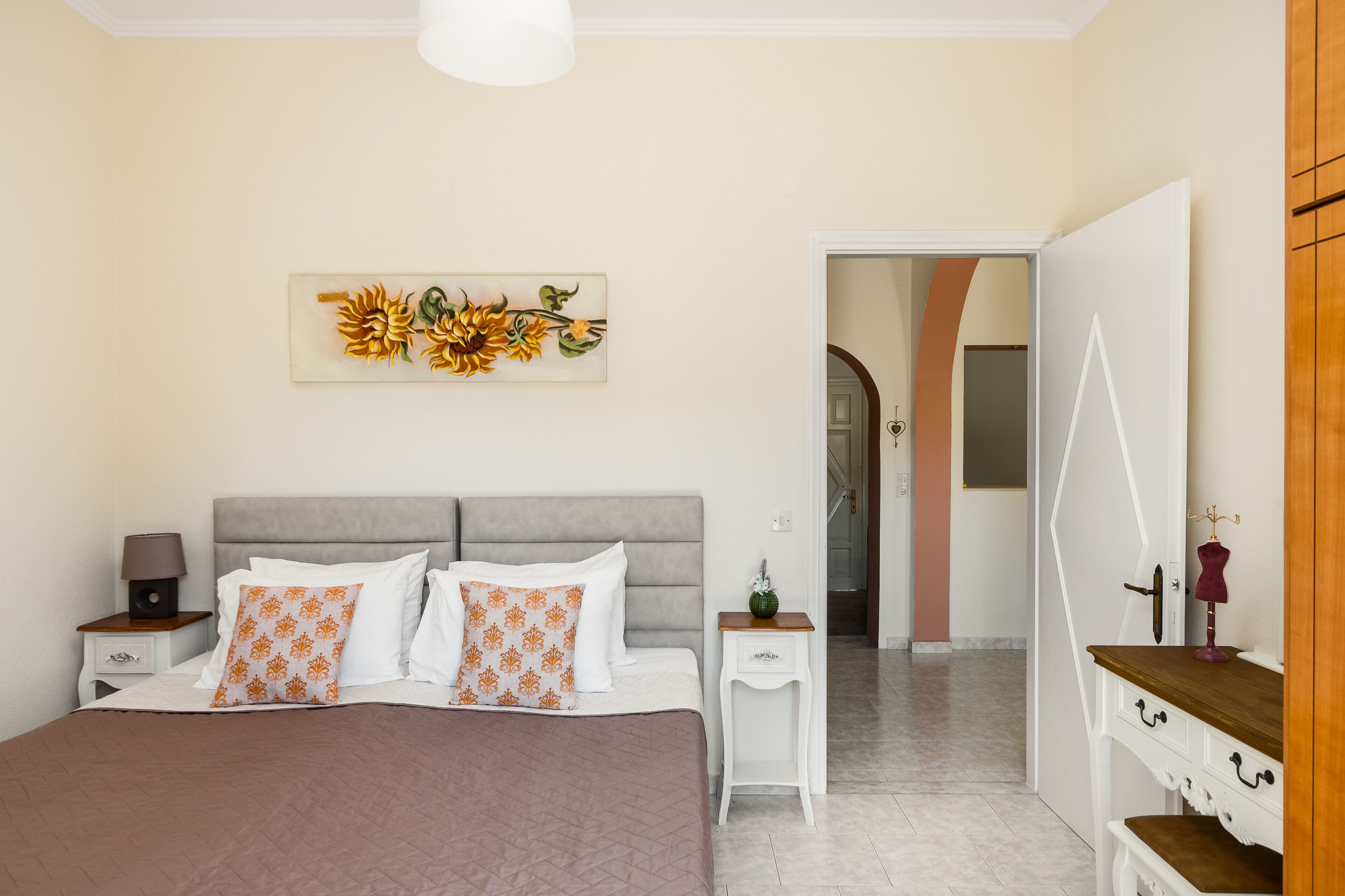 A bedroom with a large bed, two bedside tables, a nightstand, a wall-mounted artwork, and a wooden dresser.