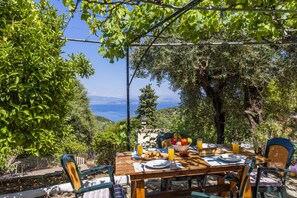 An outdoor dining area with a table set for two, surrounded by greenery and overlooking a scenic view.