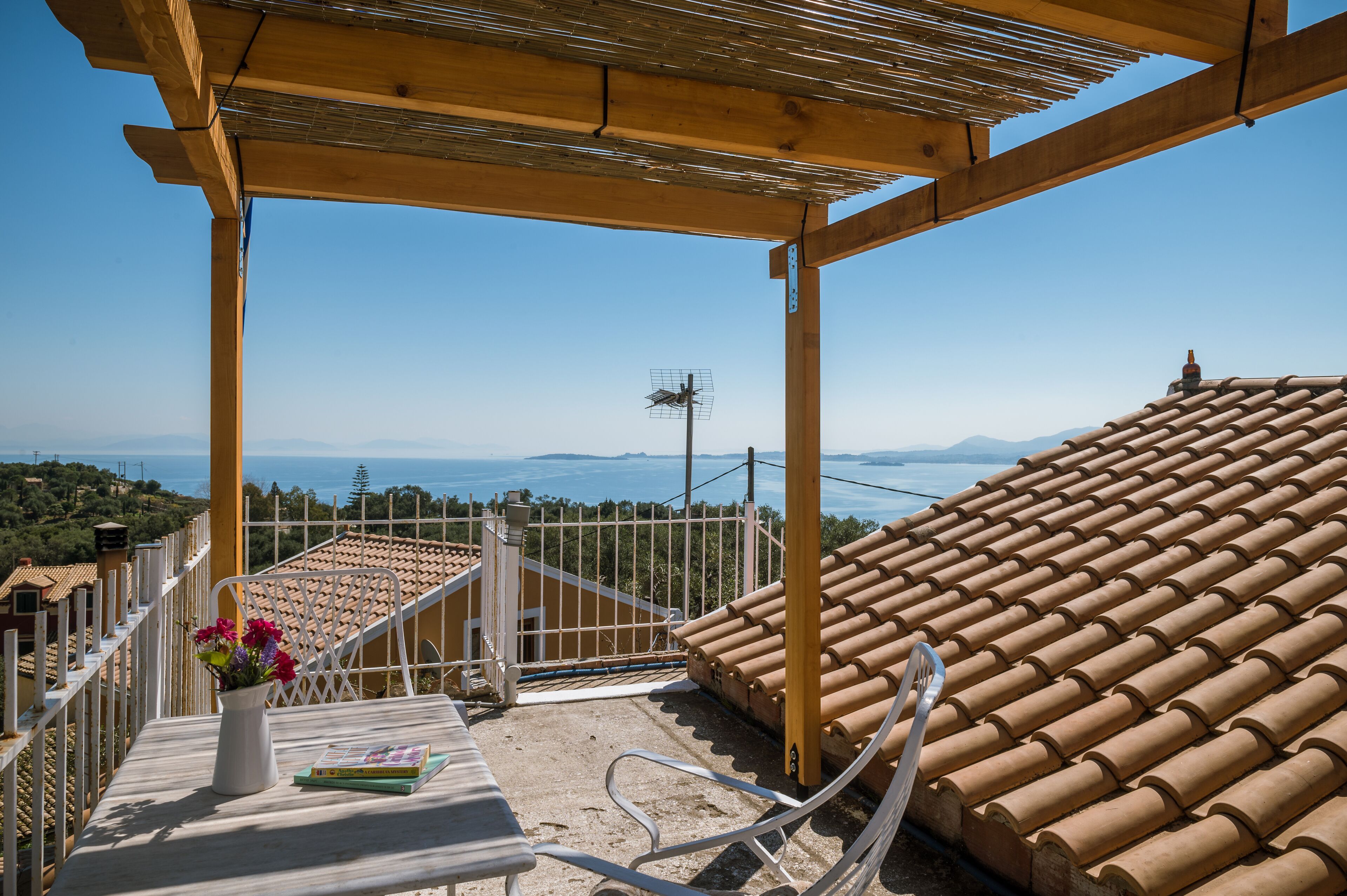 Terraza con vistas al mar y las montañas, una pérgola de madera y una silla blanca.