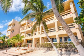 A multi-story hotel with balconies, a stone facade, and palm trees. - Tropical beachfront condo! AC, swimming pool! (Akumal)