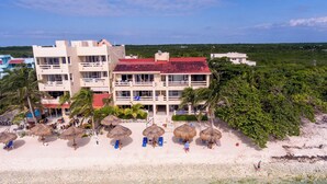 Un hotel sulla spiaggia con numerosi balconi, una zona piscina e ombrelloni.