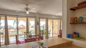 Una stanza con una porta in vetro che si apre su un balcone con vista sulla spiaggia e palme.