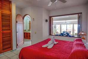 A hotel room with a large bed, a mirror, a ceiling fan, and a view of the outside. - Tropical beachfront condo! AC, swimming pool! (Akumal)
