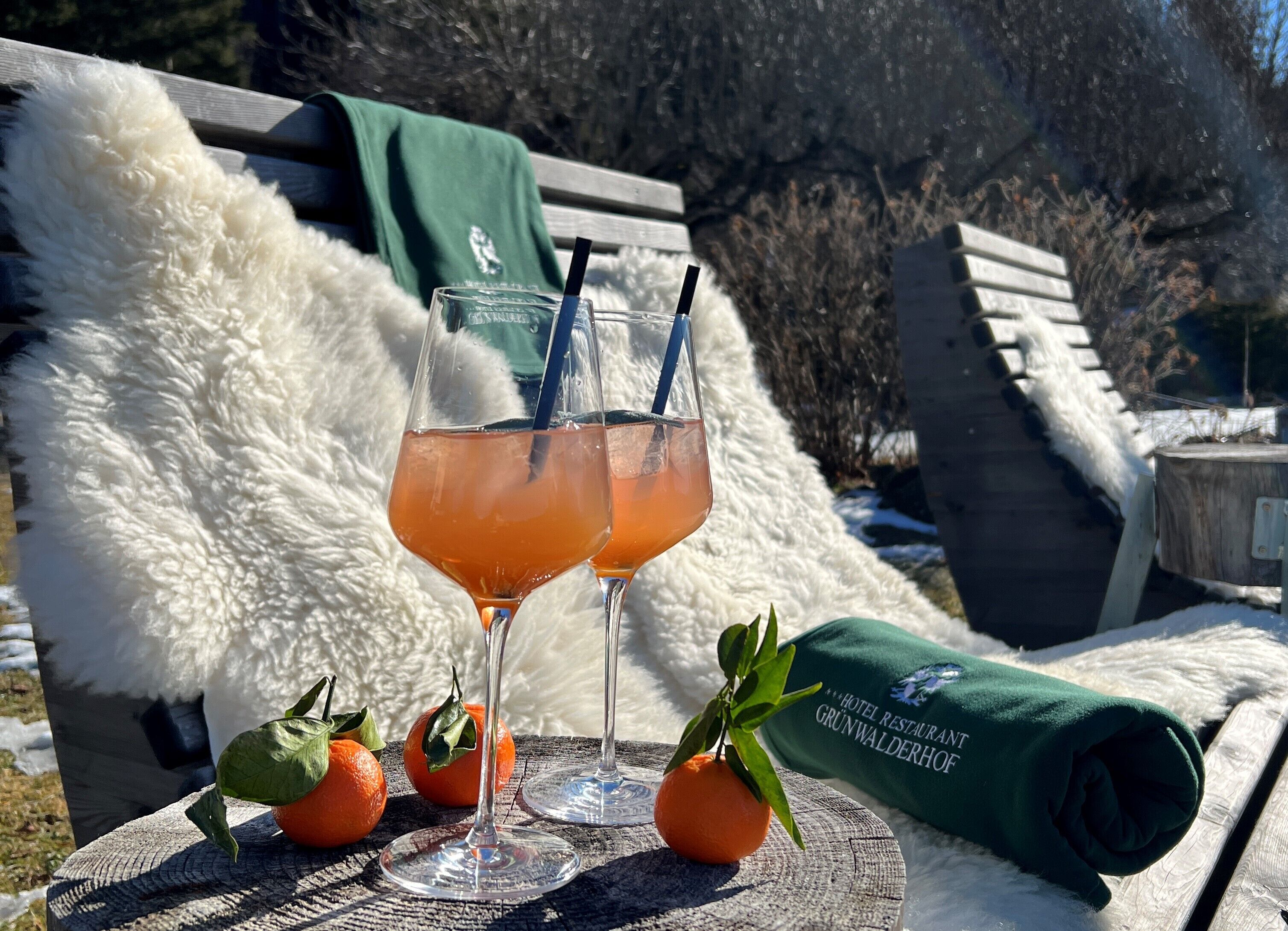 Två glas apelsinjuice står på ett träbord tillsammans med en grön handduk och två apelsiner.