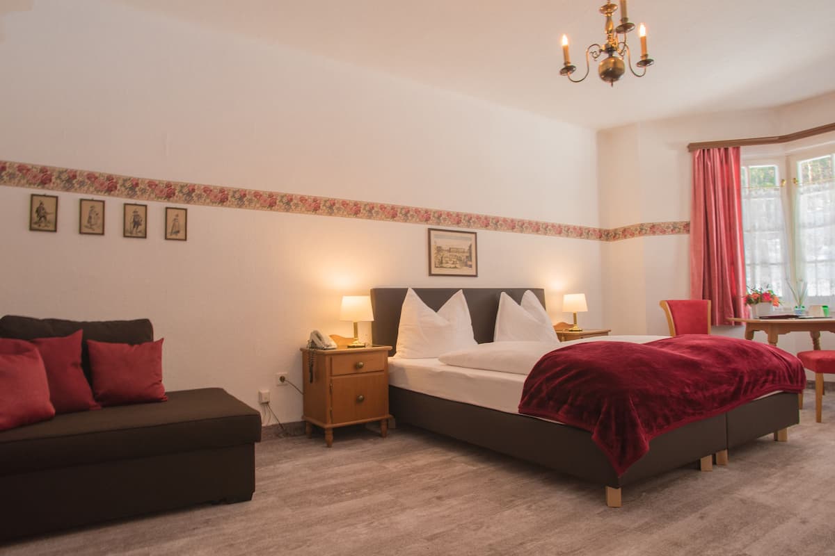 A bedroom with a bed, a nightstand, a bedside table, a chair, and a window with curtains.