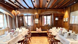 A long dining table set for a meal in a rustic room with wooden beams and large windows. - Hotel Restaurant Grünwalderhof (Patsch)