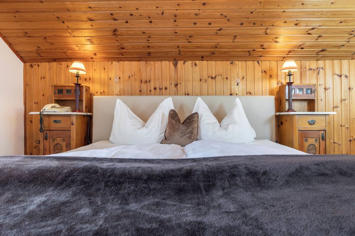 A wooden-paneled room with a bed, two nightstands, and lamps.
