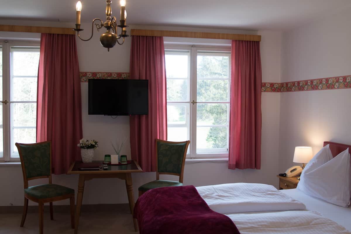A hotel room with a bed, two chairs, a table with a vase of flowers, a television, and a nightstand with a lamp and phone.