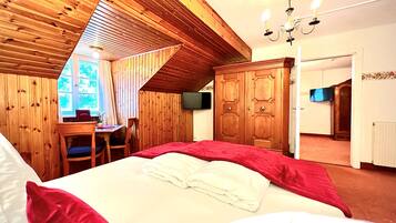 Un dormitorio con techo inclinado, paredes de madera, cama con ropa de cama roja y blanca, escritorio con silla y armario.