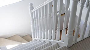 Un escalier en bois peint en blanc, doté d’une rampe, de marches recouvertes de moquette et d’une fenêtre en arrière-plan.