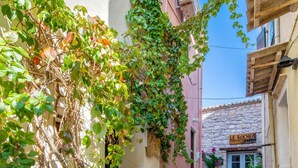 A narrow stone-paved alley with a vine-covered wall and a building entrance labeled "LE ROCHER ENFANT." - Loggos Panoramic Views Electra By Konnect (Paxos)