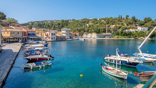 A marina with boats docked, a clear blue waterfront, and buildings in the background. - Loggos Panoramic Views Electra By Konnect (Paxos)
