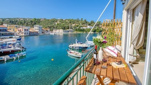 A balcony with a view of a marina, boats, and a town in the background. - Loggos Panoramic Views Electra By Konnect (Paxos)