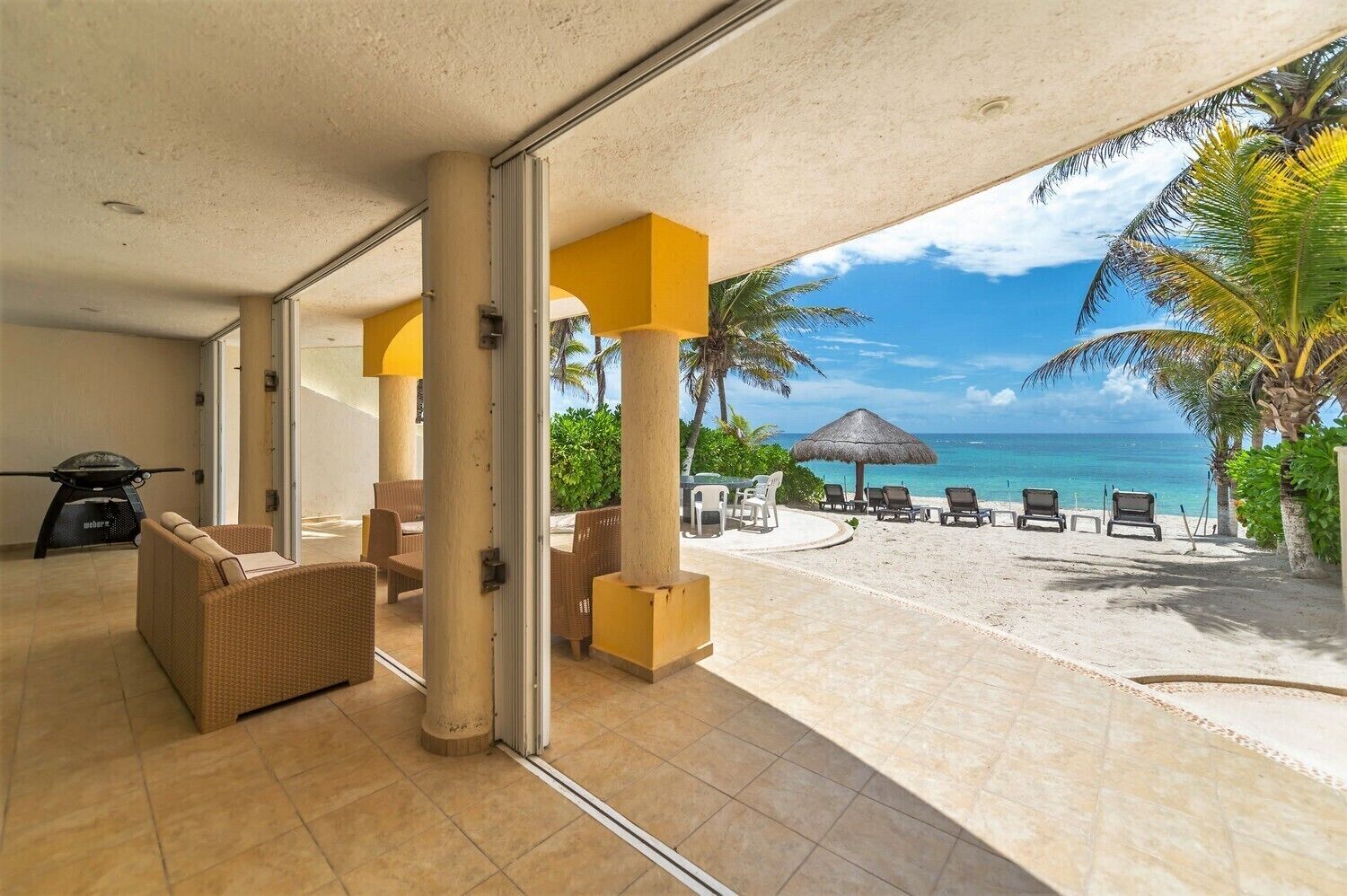 Amplia habitación con vista a la playa, que incluye una parrilla, muebles de mimbre y un paraguas de paja.