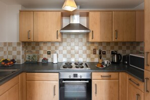 A modern kitchen with wooden cabinets, a stainless steel range hood, a built-in oven, and a black countertop.