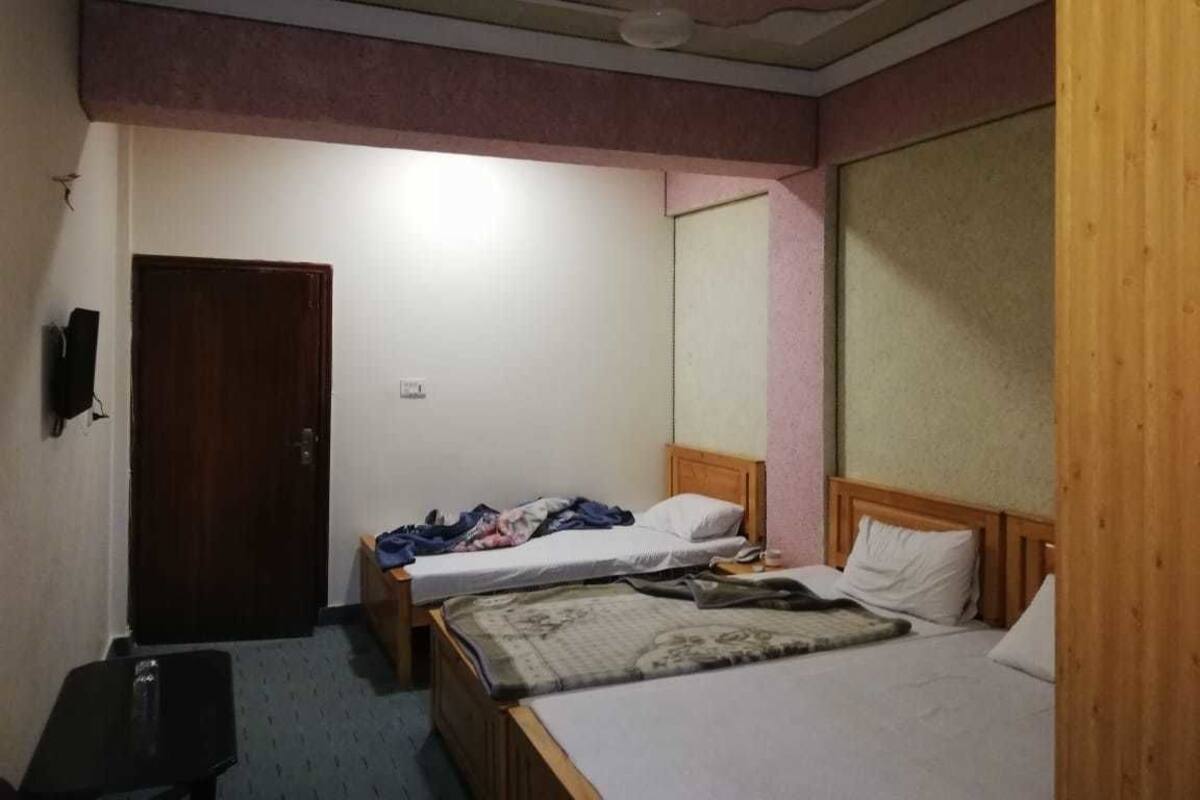 Ein Zimmer mit zwei Betten, einem hölzernen Kopfteil, einem kleinen Tisch und einer Tür.