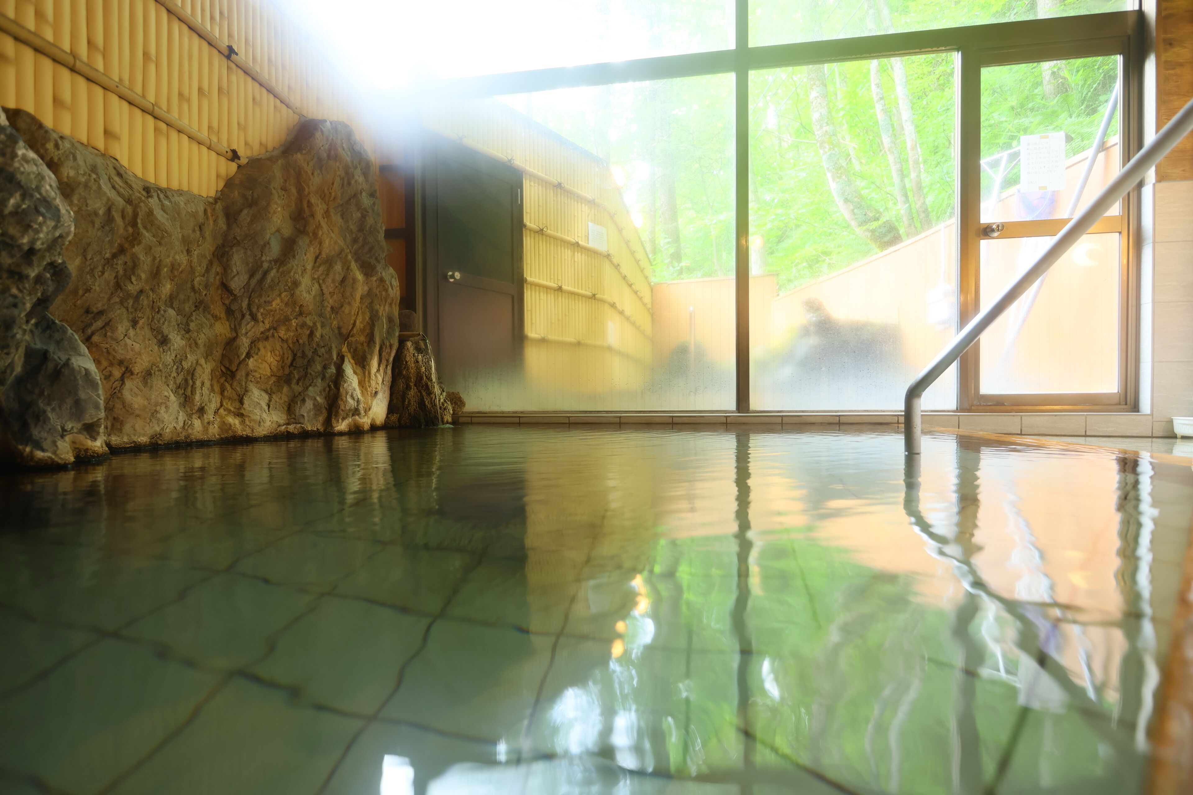 A spacious indoor swimming pool with a large rock feature and a glass door leading outside.